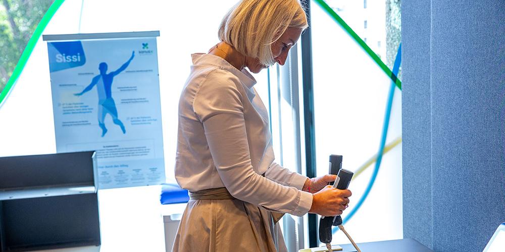 Mavie-Work Blog health-hub lifestyle-check A woman is holding the handles of a measuring device, which is part of the Mavie Lifestyle Check. This test measures 60 health parameters in approximately 20 minutes.